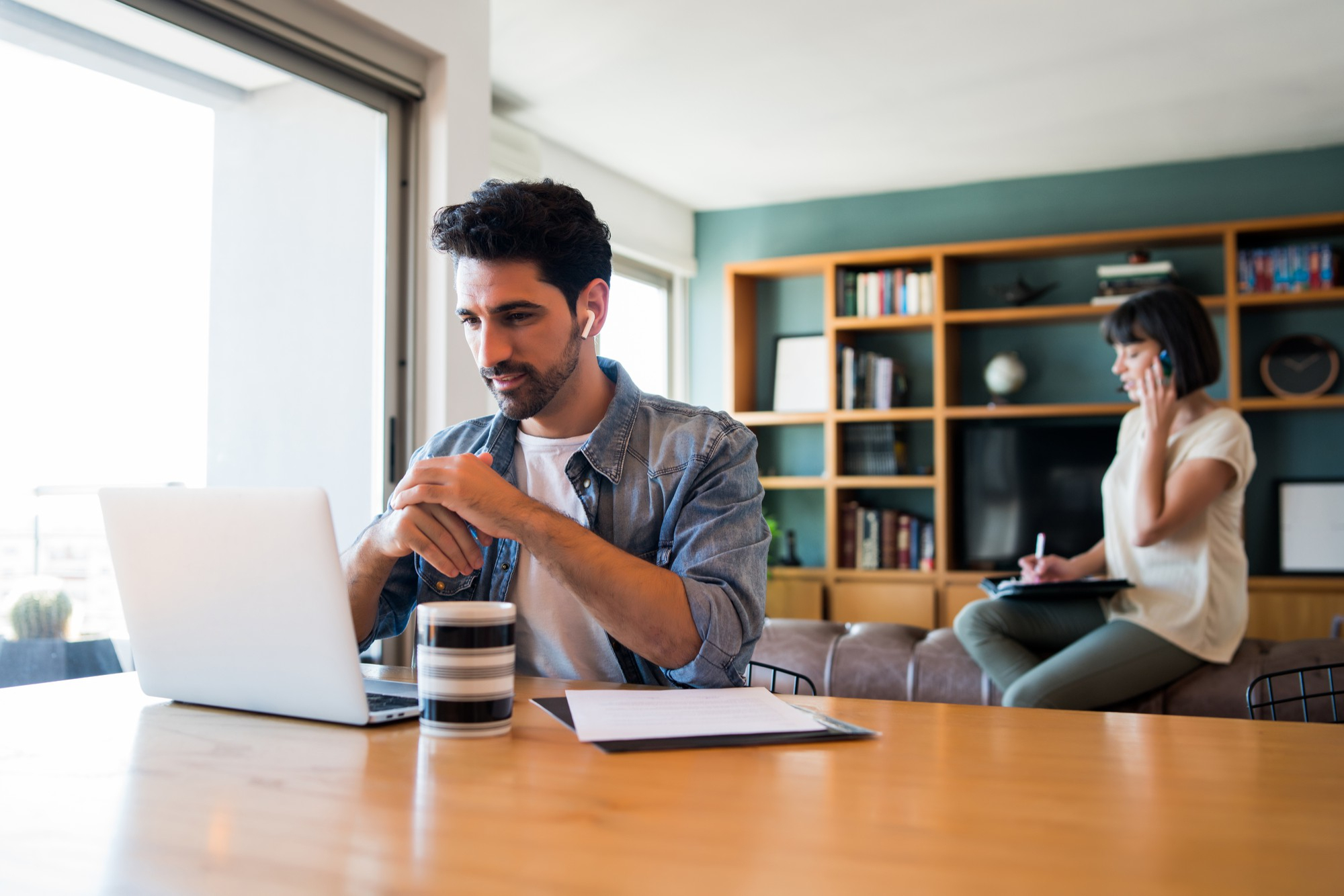 portrait-young-man-working-with-laptop-from-home-while-woman-talking-phone (1)